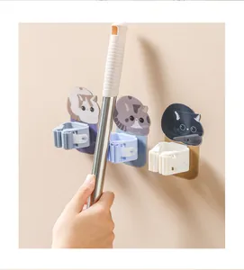 Detail view of cartoon cat self-adhesive mop holder showing a hand inserting a mop handle pole