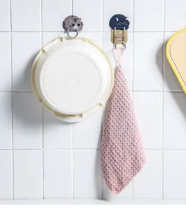 Detail view of cute cat adhesive hooks holding a washbasin and a pink towel on a tile wall