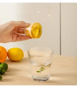 Hand holding a disposable plastic ice mold with frozen fruit over a glass of water.