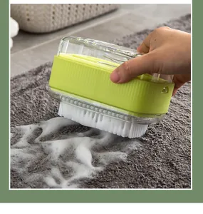 Close-up of green soap foaming box with brush scrubbing a grey carpet with white foam.
