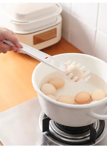 Cuillère à pâtes multifonctionnelle en plastique blanc soulevant un œuf dur d'un pot blanc