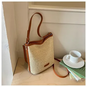 Bolso bandolera casual de paja tejida con correas de cuero marrón en un ambiente cálido