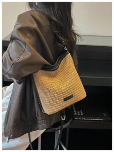 Vista detallada de un bolso bandolera de paja tejida minimalista con correas de cuero negro