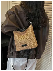 Detalle de bolso bandolera de paja tejida con correa de cuero negro sobre un modelo