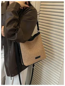 Detalle de un bolso bandolera de paja tejida con ribete negro usado por una modelo.