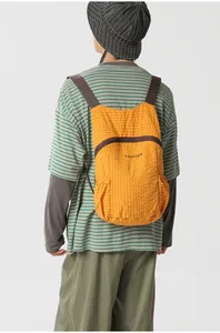 Model wearing a lightweight foldable orange plaid backpack for outdoor travel.