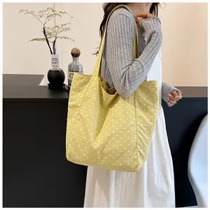 Close-up of a stylish yellow canvas tote bag with white polka dots carried by a model