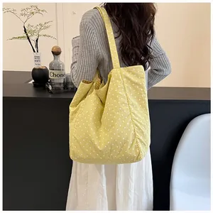 Yellow canvas tote bag with white polka dots shown in a lifestyle detail shot on a model.