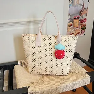 Close-up of cream polka dot tote bag with a cute strawberry charm on a woven chair