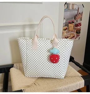 Detailed shot of white polka dot tote bag featuring a cute strawberry charm on a chair