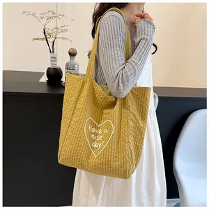 Close-up of a yellow canvas tote bag with white heart embroidery and 'Have a nice day' text