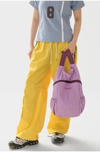 Detailed view of a lightweight purple plaid folding outdoor backpack held by a model outdoors.