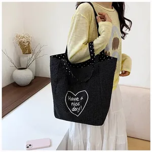 Detail of the black checkered canvas tote bag featuring a white heart design and polka dot strap