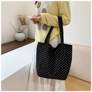 Close-up detail of a stylish black and white polka dot canvas tote bag worn by a model