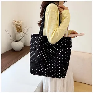 Large black canvas tote bag with white polka dot pattern shown carried by a model