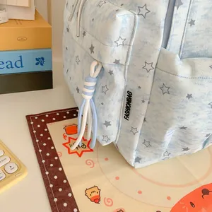 Close-up detail of light blue star pattern backpack featuring woven cord tassel and brand label