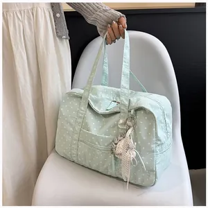 Mint green polka dot Boston travel bag held by hand against a white chair for detail view