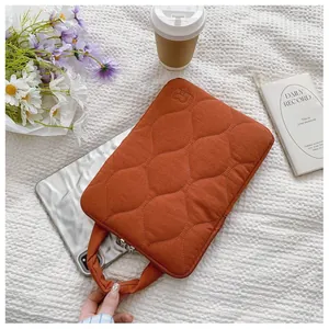 Gros plan d'une housse d'ordinateur orange matelassée avec poignée sur fond blanc texturé