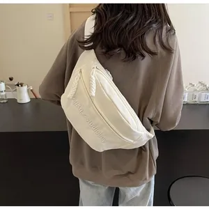 Back view of a cream canvas crossbody chest bag on a person in a minimalist cafe