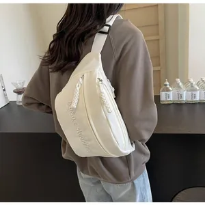 Back view detail of a white minimalist crossbody bag with embroidered text on nylon fabric