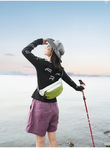 Rückansicht einer grün-weißen Outdoor-Brusttasche, getragen von einer Wanderin am See