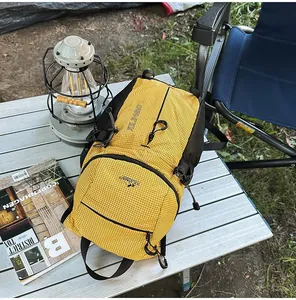 Mochila de senderismo amarilla impermeable sobre una mesa de camping con un farol al aire