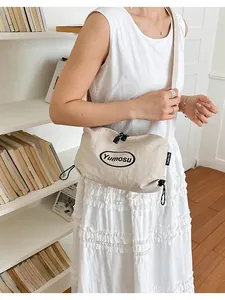 Detail view of a lightweight minimalist beige crossbody bag worn with a white dress