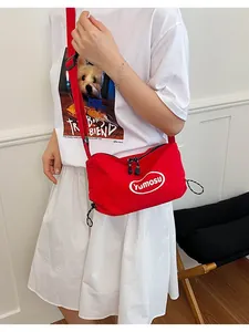 Detailed view of a trendy red lightweight crossbody bag worn over a white dress outfit.