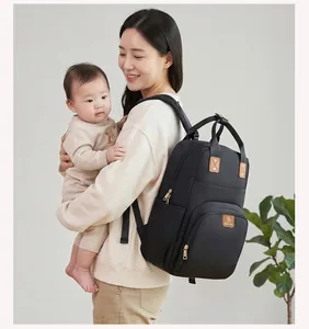 Madre asiática con mochila de pañales negra mientras sostiene a su bebé