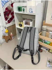 Detailed rear view of minimalist light grey nylon backpack with adjustable straps on a desk