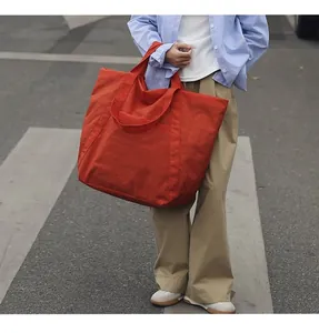Modell trägt eine große orangefarbene Nylon-Einkaufstasche im lässigen Streetstyle.