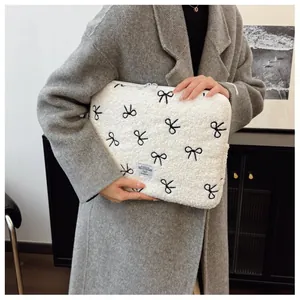 Detailweergave van een witte pluche laptoptas met zwart geborduurde strikpatronen