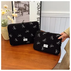 Gedetailleerde weergave van twee zwarte pluche laptophoezen met witte strikborduursels