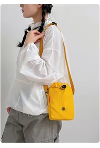 Vista detallada de un bolso bandolera amarillo vibrante para móvil y botella en un modelo.