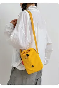 Bolso bandolera amarillo brillante con cordón para móvil usado por una modelo de forma casual