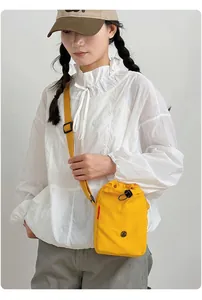 Vista detallada del bolso bandolera amarillo de nailon lucido por una modelo vestida de blanco
