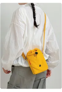 Detalle de un bolso bandolera de nailon amarillo con cierre de cordón llevado por modelo.