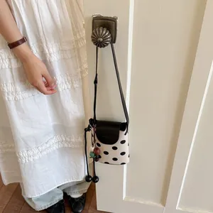 Detailed view of black and white polka dot mini bucket bag with leather flap and hanging beads.