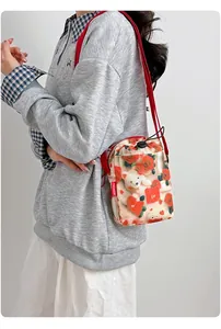 Modelo luciendo un pequeño bolso bandolera para móvil con estampado de rosas y oso.