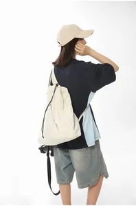 Back view of a female model carrying a large minimalist cream nylon drawstring shoulder bag