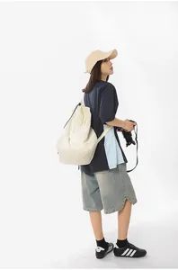 Side back view of a model showcasing the large cream nylon drawstring tote bag