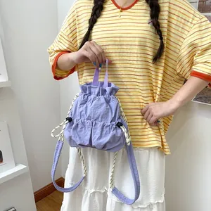 Detailansicht eines lila wasserdichten Nylon-Rucksacks mit Kordelzug, von einem Model gehalten.