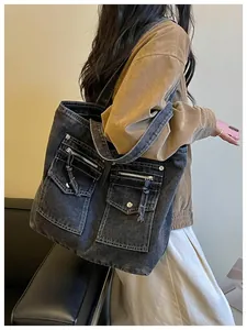 Detail view of large grey denim tote bag with functional multi-pockets worn by model