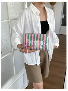 Detailed view of a glossy pink and green striped cosmetic bag featuring a pink wrist strap.