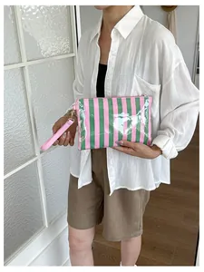 Model holding a stylish pink and green striped cosmetic bag with glossy leather finish.