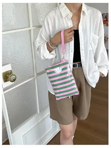 Woman holding a pink and green striped cosmetic pouch in a minimalist indoor setting