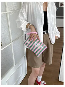 Detail of a pink and green striped travel cosmetic bag held by a model in a white shirt