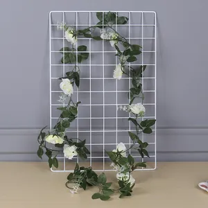 Detail view of an artificial white rose vine garland hanging on a white grid panel