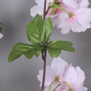 Gros plan détaillé des pétales de fleurs de cerisier en soie rose et des feuilles vertes.