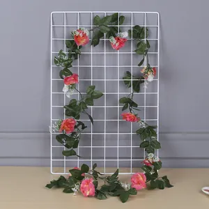 Close-up of pink artificial rose vine with green leaves on a white grid display